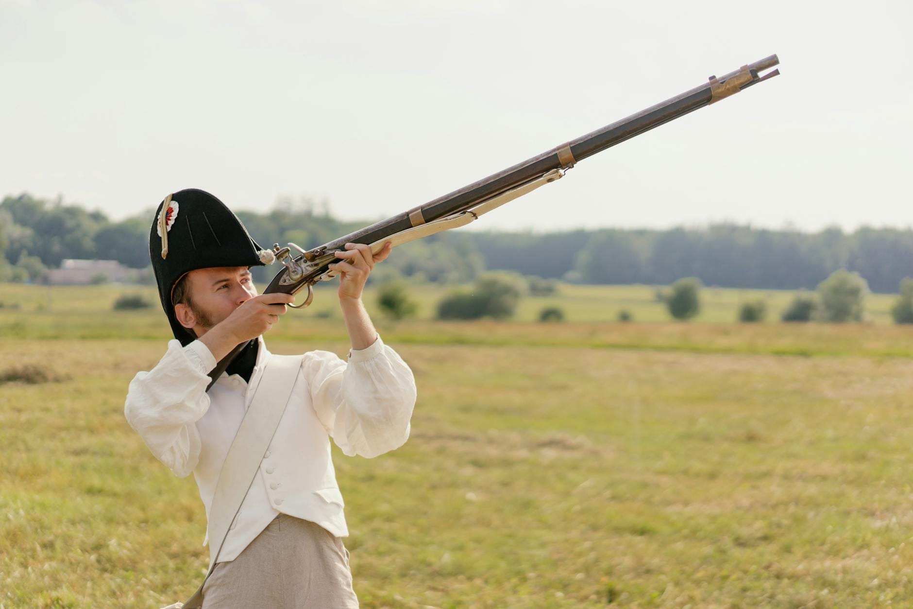 Rekonstruktor historyczny w stroju z epoki celuje z muszkietu na polu