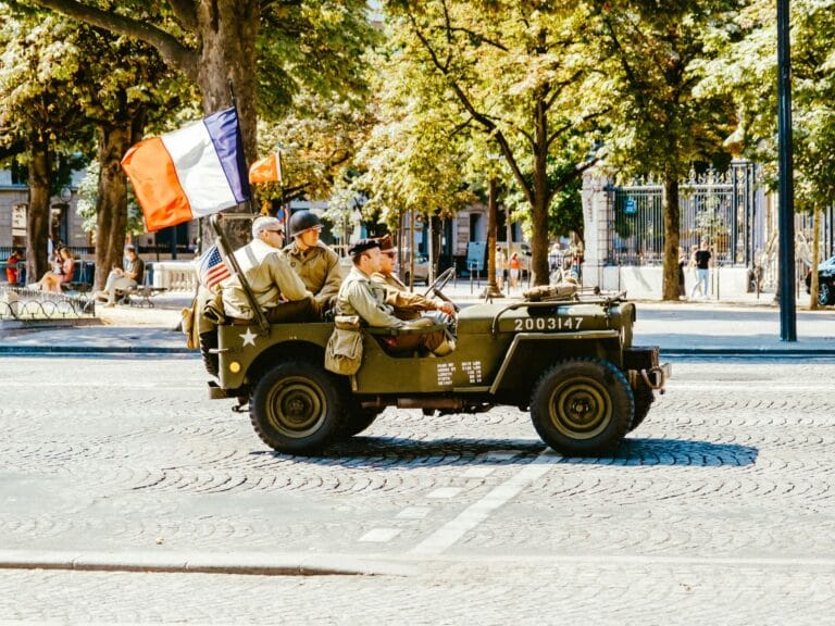 Zabytkowy wojskowy jeep z żołnierzami i flagami Francji oraz USA na paradzie
